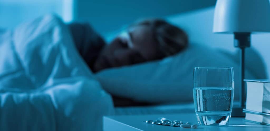 Person sleeping with sleeping pills on a bed table